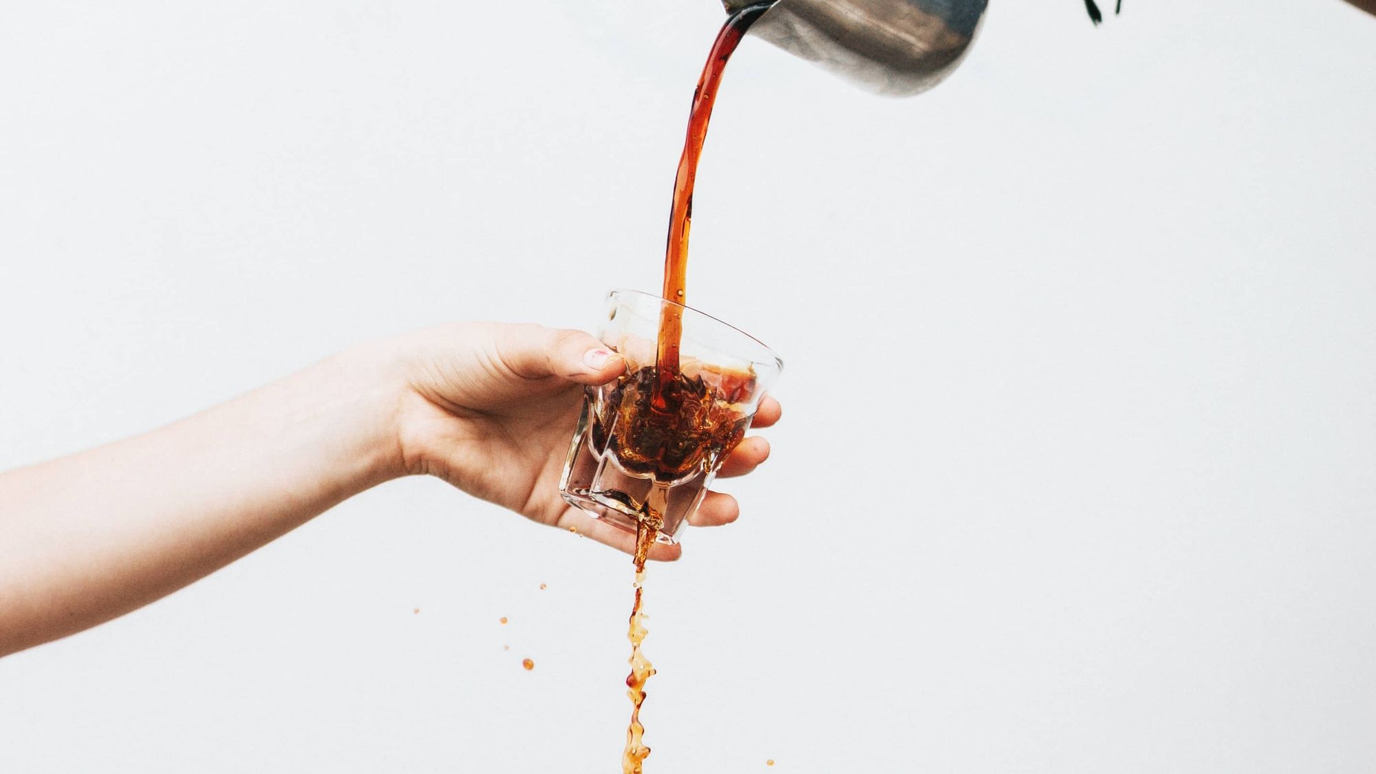 hand holding a glass into which coffee is poured